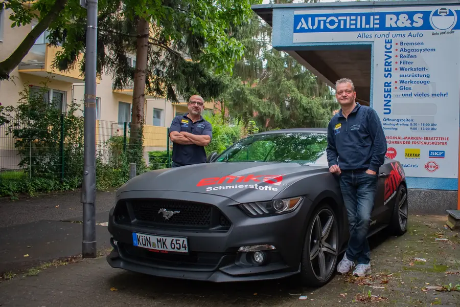 Die beiden Inhaber mit ihrem Ford Mustang vor dem Ladenschild an der Zehnthofstraße